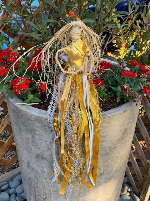 A silver and gold Wheat dolly sits among flowers